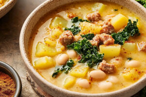A bowl of creamy Tuscan soup with kale, sausage, potatoes, and a rich, flavorful broth, garnished with Parmesan cheese.